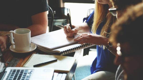 Four people sit at a table with a computer and notebooks