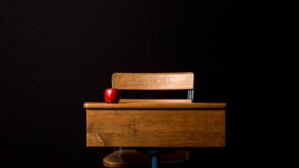 An apple sits on an empty wooden desk before a black backdrop
