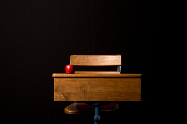 An apple sits on an empty wooden desk before a black backdrop