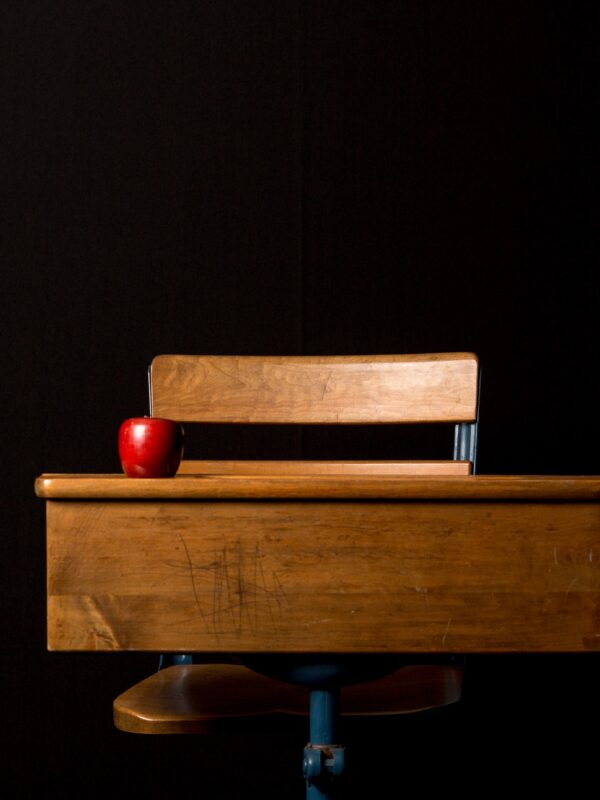 An apple sits on an empty wooden desk before a black backdrop