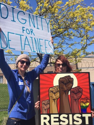 protesters hold signs saying "dignity for detainees" and "resist"