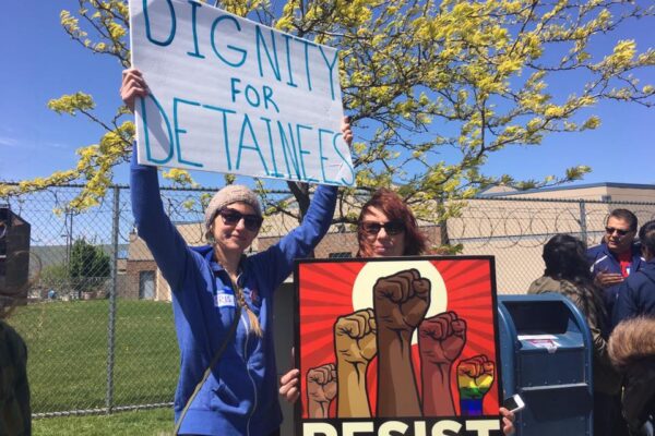 protesters hold signs saying "dignity for detainees" and "resist"