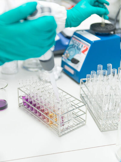 A gloved hand injects fluid into a test tube.