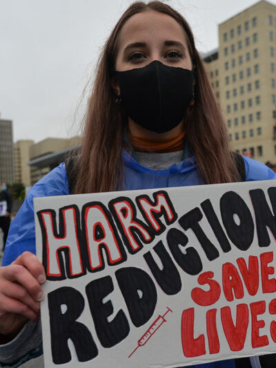 Edmontonian with a sign that reads "harm reduction saves lives," photos of loved ones and crosses with purple ribbons and hearts gather for International Overdose Awareness Day at Capital Plaza outside the Federal Building.