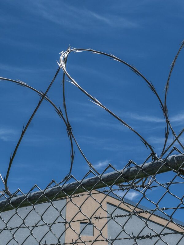 Close up image of a prison fence with barbed wire at the top glinting in the sun