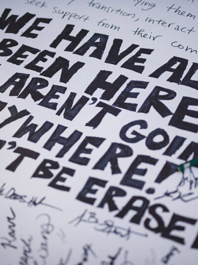 A demonstration poster that reads “We Have Always Been Here! We Aren’t Going Anywhere! We Won’t Be Erased.”