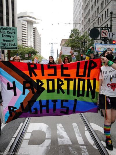 People holding a rainbow flag banner reading "Rise Up 4 Abortion Rights" while marching at the 2022 San Francisco Pride parade of 2022.