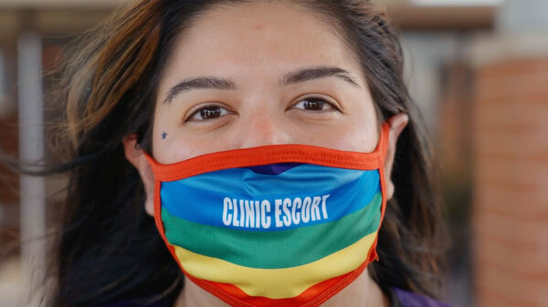 A close-up of Mariceli Alegria who's wearing a rainbow facemask with the printed words "Clinic Escort".