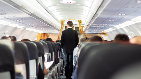 A flight attendant wearing a suit walking through the aisle of a plane.