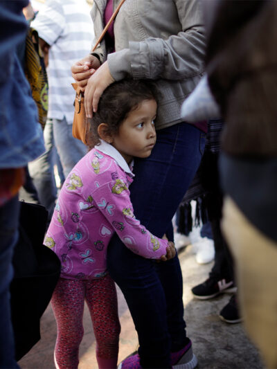 A young child holds on to her mother legs as they wait with other families to request political asylum in the United States, across the border in Tijuana, Mexico.