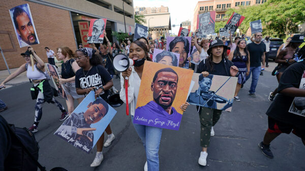 Protestors walking down the street, with one holding a microphone and a sign with art of George Floyd's face.