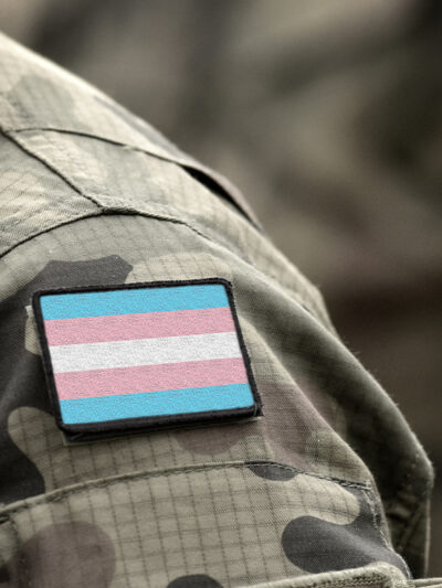 Transgender Pride flag on shoulder of a military camouflage uniform.