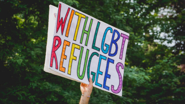 A hand holding up a "With LGBT Refugees" sign.