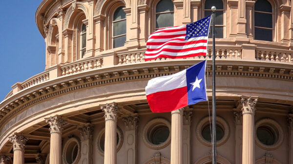 American and Texas state flags flying on the dome of the Texas State Capitol building.