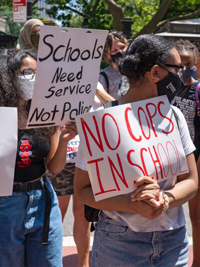 Demonstrators holding signs that read "No Cops In Schools" and "Schools Need Service Not Police" protest outside City Hall in New York City.