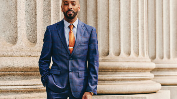 Daudi Justin standing in front of a marble column with his left hand in his pant pocket.