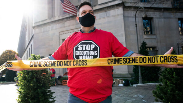 Man protesting against the death penalty in fron of the U.S. Justice Dept wearing a red shirt with a black stop sign reading "STOP EXECUTIONS NOW" in white letters.