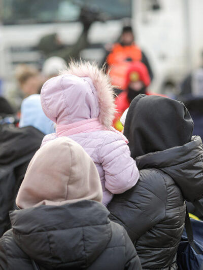 The back of a group of individuals, one holding a child with a hooded coat on.