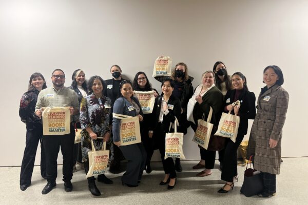Members of the ACLU, Basic Rights Oregon, Oregon Education Association and the Oregon Library Association grouped together holding tote bags that say "I survived reading banned books and all I got was smarter."