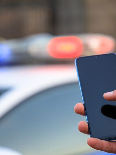 Hand holding phone with police car lights shining in the background.