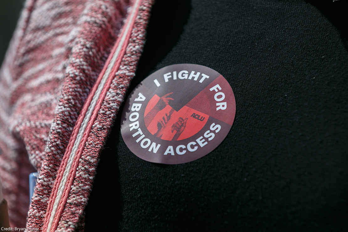 Someone wearing a sticker that says "I Fight For Abortion Access."