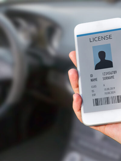 A hand (within a car) holding a cellphone displaying a digital drivers license.