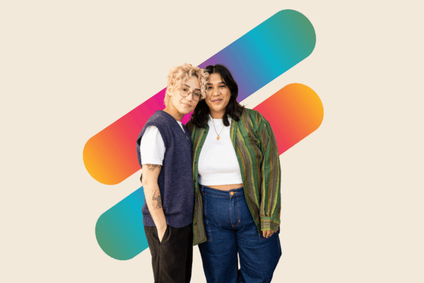 A queer appearing couple with their arms around each other in front of two thick lines with a rainbow color gradient.