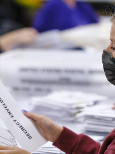 A woman with a surgical mask opening absentee ballots.