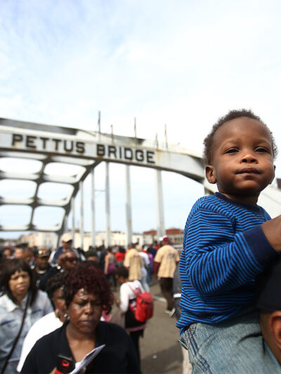 An infant sits atop His Father's Shoulders As Marchers Cross the Edmund Pettus Bridge During the 50th Anniversary Commemoration of the 'Bloody Sunday' Crossing of the Bridge in Selma Alabama.