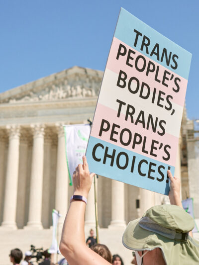 A demonstrator at a march in front of the Supreme Court holds up a sign reading "TRANS PEOPLE'S BODIES, TRANS PEOPLE'S CHOICES".
