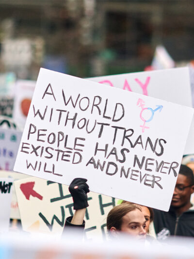 A pesron holding up a sign reading "A World Without Trans People Has Never Existed And Never Will" at a demonstration.