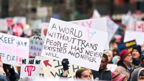 A pesron holding up a sign reading "A World Without Trans People Has Never Existed And Never Will" at a demonstration.