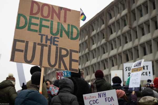 People attend a rally against the Trump administration's 90-day funding freeze and job cuts at health agencies in Washington, DC, hold up a large sign written in red, green and black on cardboard that reads " DON'T DEFUND THE FUTURE."