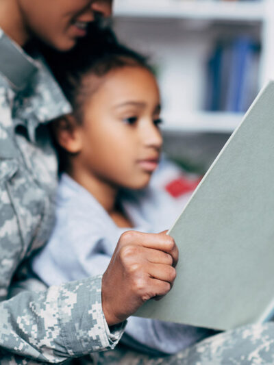 A mother in a military uniform reading to her daughter.