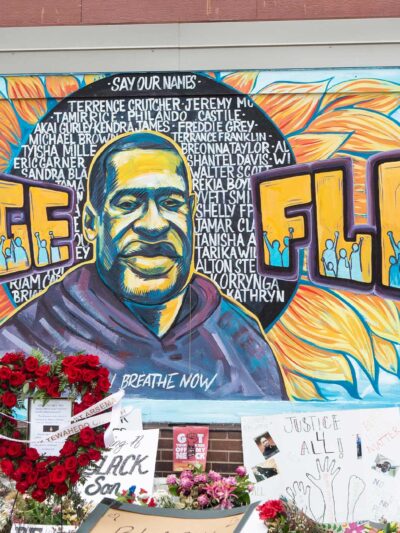 A mural with the image of George Floyd ihas flowers and signs protesting his murder lay beneath it five years later.