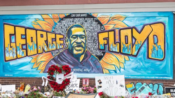 A mural with the image of George Floyd ihas flowers and signs protesting his murder lay beneath it five years later.