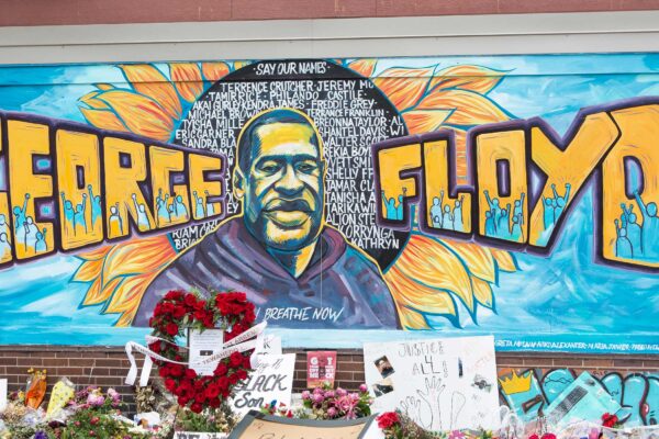 A mural with the image of George Floyd ihas flowers and signs protesting his murder lay beneath it five years later.