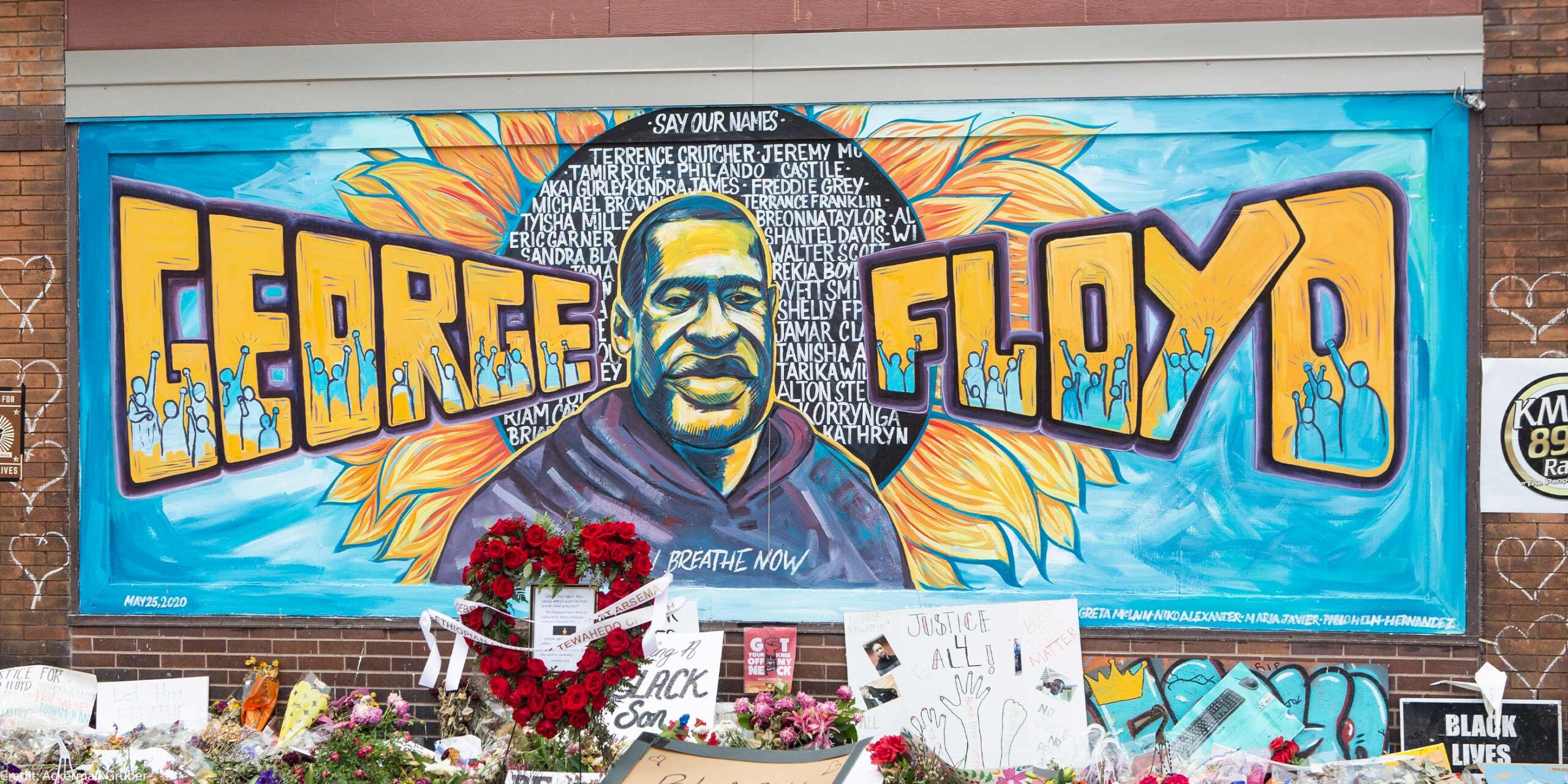 A mural with the image of George Floyd ihas flowers and signs protesting his murder lay beneath it five years later.