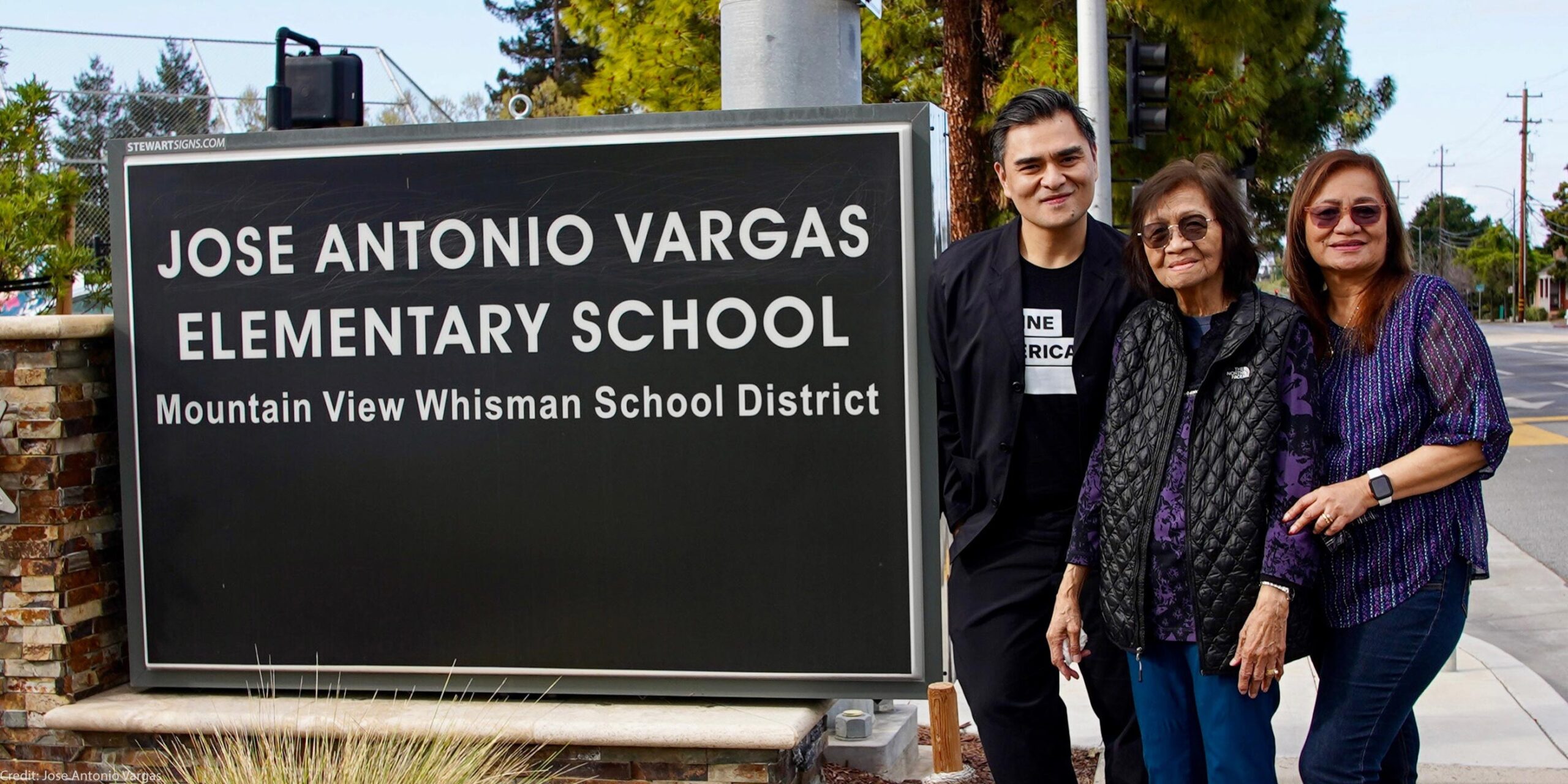 A smiling Jose Antonio Vargas and two equally joyful female family members stand to the right of a large sign that reads "JOSE ANTONIO VARGAS