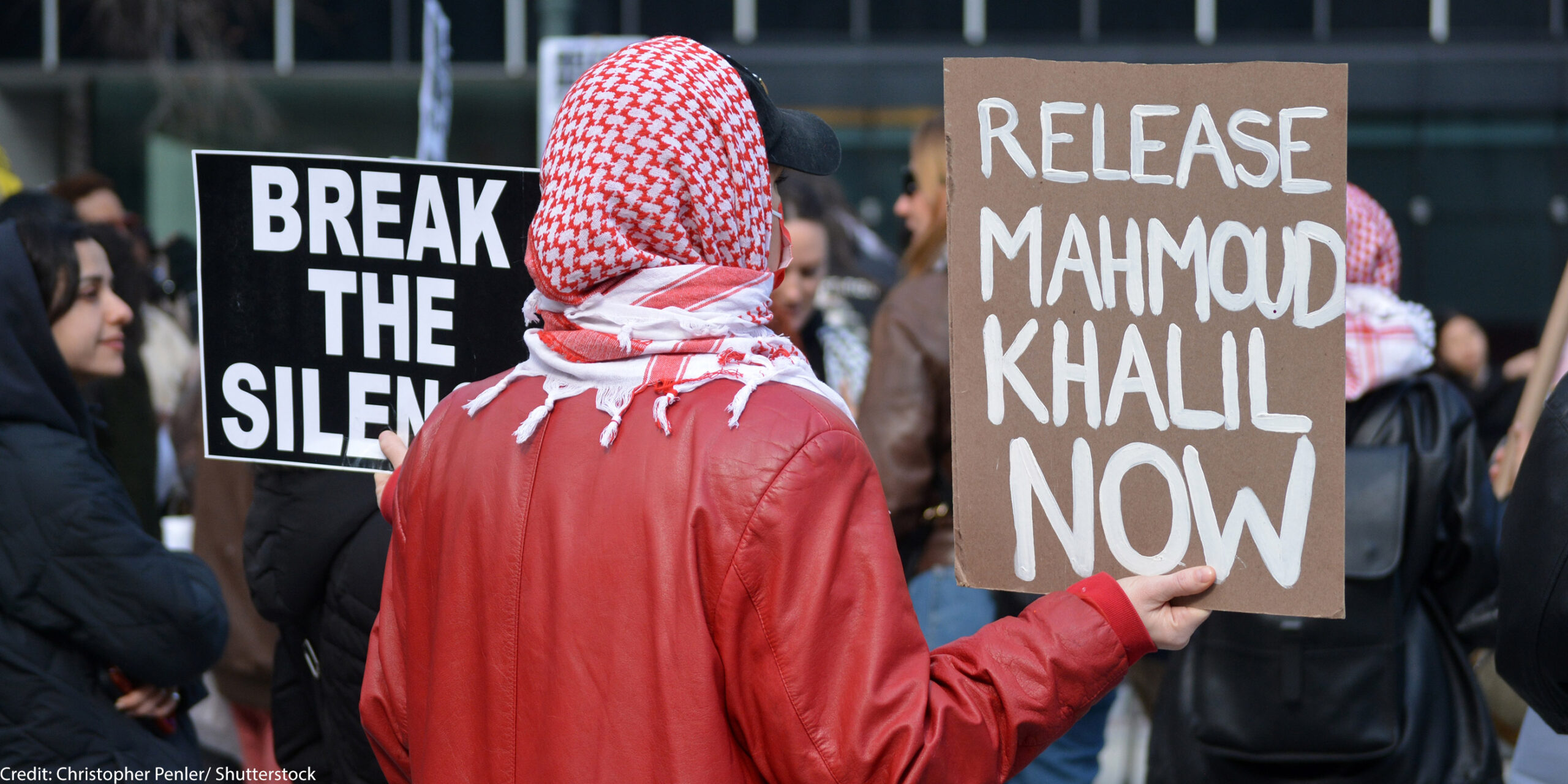 A student activist holding a sign that says "Release Mahmoud Khalil Now."