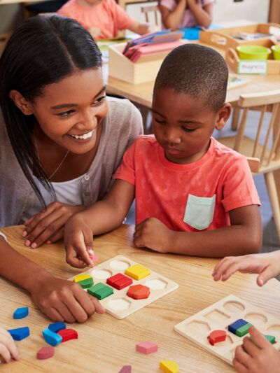 Teacher and pre-K students using wooden shapes.