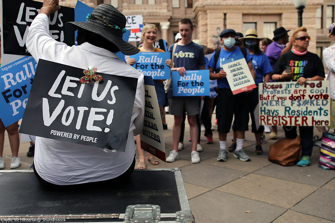 And group of demonstrators, one with a sign taped to their back saying "Let Us Vote!"
