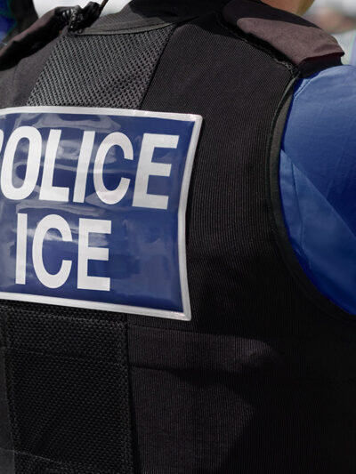 Close-up of POLICE ICE marking on the back of a vest uniform worn by a trio of officers.
