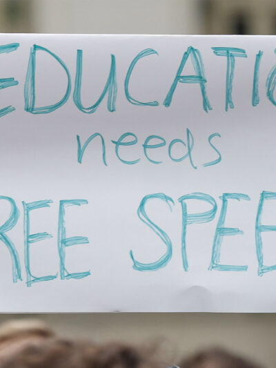 A student holds up a placard reading 'Education needs free speech' while attending a march.
