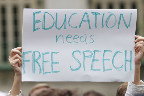 A student holds up a placard reading 'Education needs free speech' while attending a march.