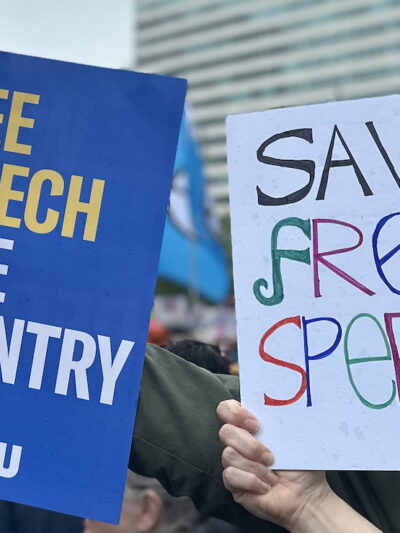 One protest sign reads: "Free Speech, Free Country." The other reads: "Save Free Speech"