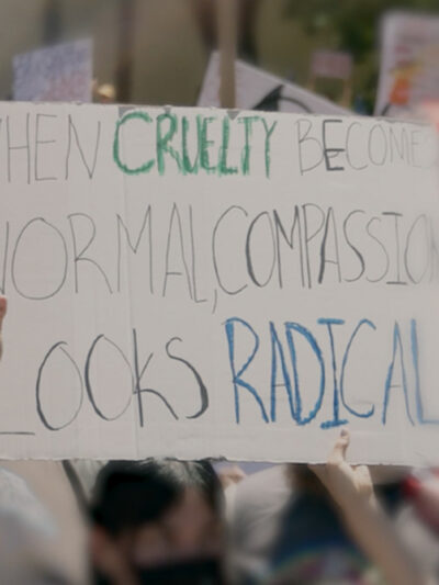 A demonstration sign that say "When Cruelty Becomes Normal, Compassion Looks Radical."