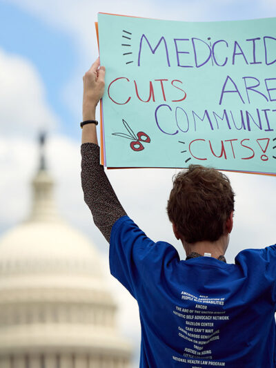 An individual at a 24-hour Vigil and Rally to Protect Medicaid on Capitol Hill, outside of the U.S. Capitol Building, holding a sign that says "Medicaid Cuts Are Community Cuts."