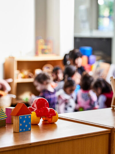 Toys in the forefront and preschoolers (blurred out) in class in the background.