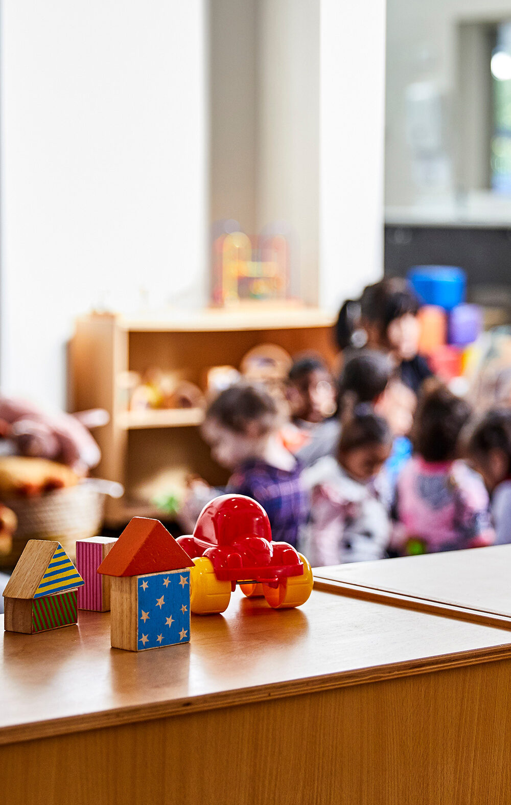 Toys in the forefront and preschoolers (blurred out) in class in the background.